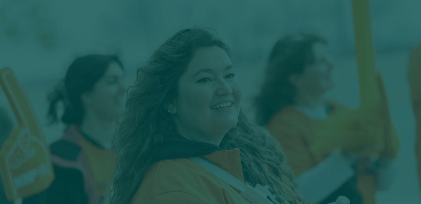 A person participating in BMO Walk so Kids can Talk, in an orange jacket looking over their shoulder while holding a water bottle, with others standing blurred in the background under a green-tinted overlay.