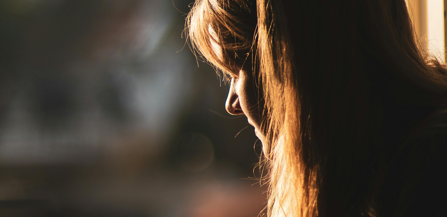 A close-up side view of a person’s face and long hair, illuminated by warm sunlight against a softly blurred background.