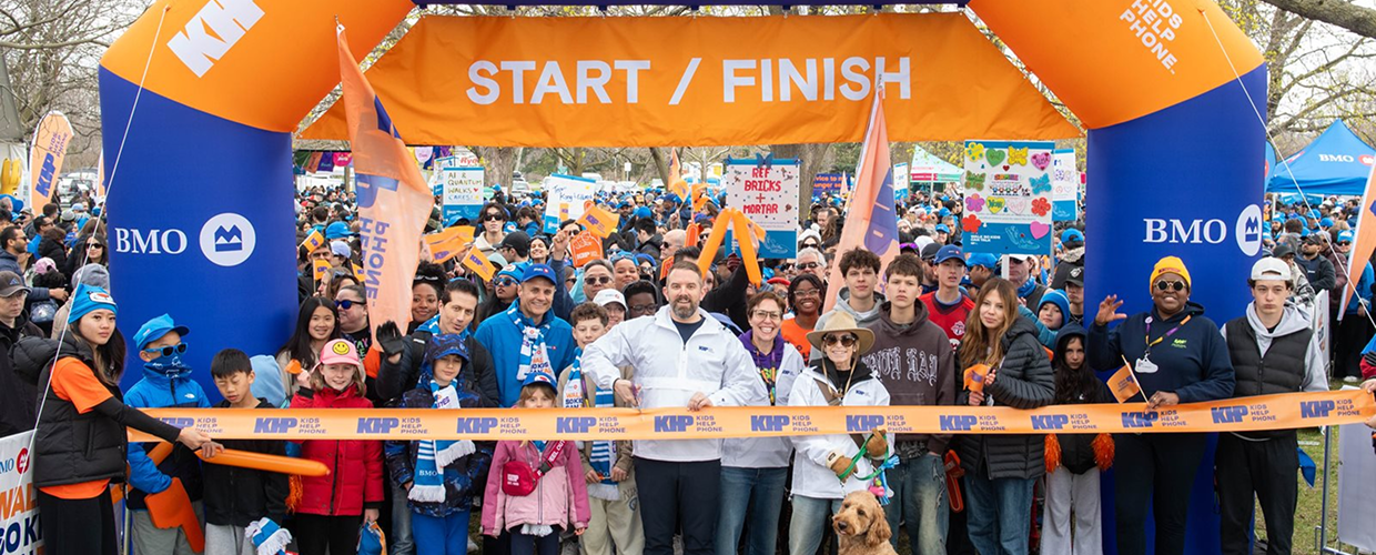 A large crowd gathers at a start/finish line banner for BMO Walk so Kids Can Talk.